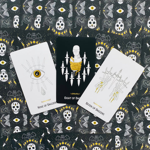 Tarot kortos su daggers rūšimi: trys atverstos kortos (Seven, Eight, Nine) prieš juodai geltoną ornamentinį foną