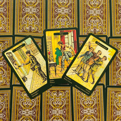 tarot kortos klasikiniu ornamentu nugarėlių fone, trys atverstos geltonai–žalsvos iliustruotos kortos matomos iš arti