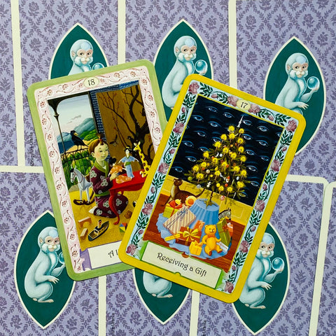 tarot kortos – dvi atverstos Urania ilgos kortos, viena su dovanų scena ir eglute, kita su vaikystės žaidimais ant violetinės nugarėlės