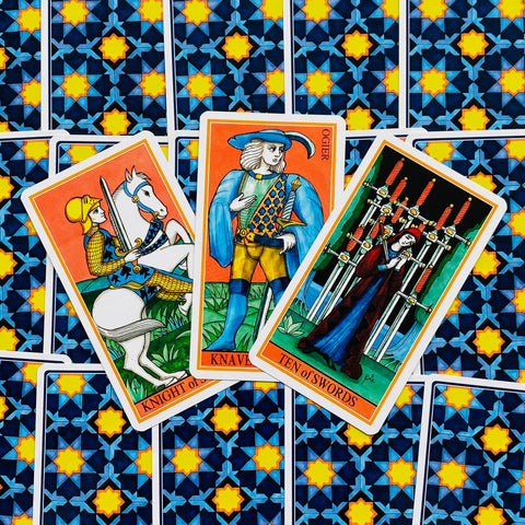 Tarot kortos su ryškiais oranžiniais rėmeliais, trys atverstos kortos virš mėlynos nugarėlės su geltonomis žvaigždėmis