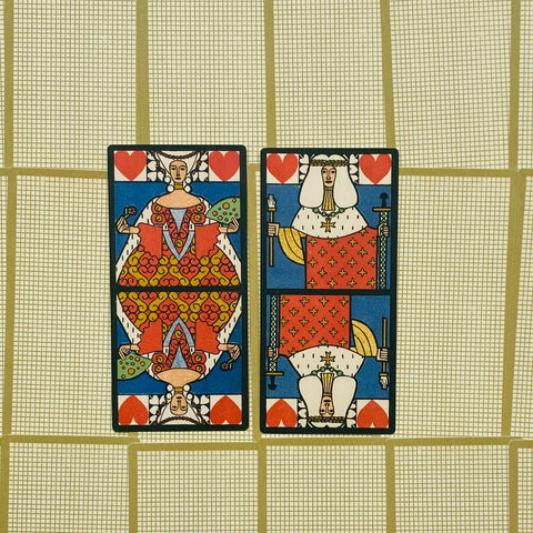 tarot kortos – dvi atviros raudonai‑mėlynos karališkos kortos (karalienė ir karalius) iš viršaus ant auksinio tinklelio fono