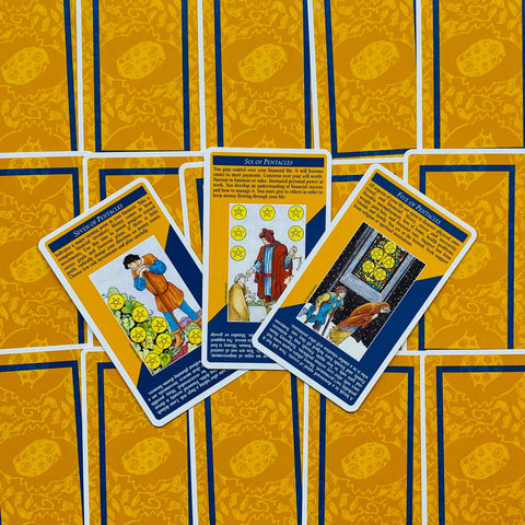 tarot kortos su geltonu nugarėlių raštu – trys Pentaklių kortos padėtos skersai, demonstruojančios 5., 6. ir 7. pentaklių reikšmes