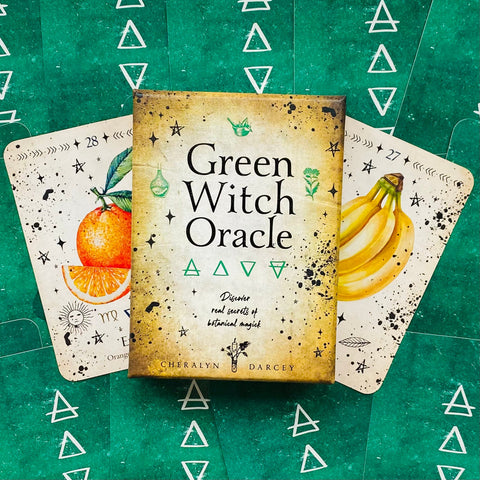 Orakulo kortos Green Witch — žaliame dėkle su botaniniu dizainu, parodyta dėžutė ir dvi kortos (apelsinas, bananas)