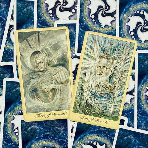 Tarot kortos su atvertomis Two of Swords ir Three of Swords kortomis, smulkiai iliustruotomis pastelinėmis spalvomis ir mėlynais nugarėlių raštais