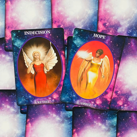 Angelų oracle kortos ant kosminio fono, dvi atviros kortos iš viršaus: Vretiel (raudona suknelė, indecision) ir Cassiel (geltona su šviesa, hope)