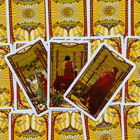Tarot kortos su geltonai auksiniu nugarėlių raštu, trys priekinės kortos (2, 3 ir 4 Lazdelės) išrikiuotos ant dugno tekstūros, pabrėžiant priekinių iliustracijų detales