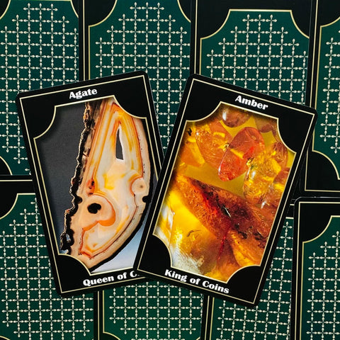 tarot kortos artimas planas: Agate ir Amber kortos su akmens motyvais, geltoni ir smėlio atspalviai ant žalios raštuotos nugarėlės