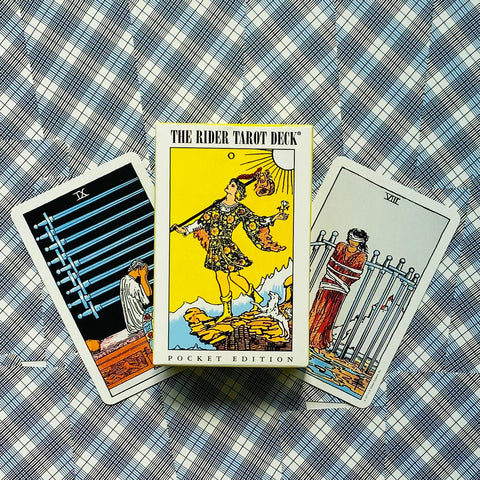 Produkto nuotrauka: The Rider Tarot pocket edition dėžutė priekiniu kampu, šone matomos Devyni ir Aštuoni kardai kortos ant mėlyno languoto fono