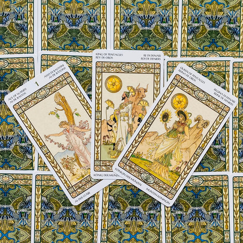 Tarot kortos su Art Nouveau iliustracijomis — trys atverstos kortos ant ornamentuotų nugarėlių, matomos iš viršaus