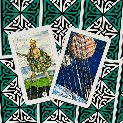 Tarot kortos, dvi atviros ir šiek tiek persidengusios: 7 lazda su škotišku pledu ir kosminė 8 lazda ant žaliai‑juodų nugarėlių