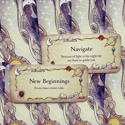 Orakulo kortos su pastelinėmis iliustracijomis, dvi atviros kortos („New Beginnings“ ir „Navigate“) horizontaliai ant žvaigždėto fono, pristatomos kaip įžanginis variantas