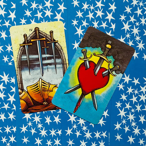 tarot kortos – ryškūs peiliai ir įmerktas širdies motyvas ant mėlyno žvaigždėto nugarėlio, skirtingi priekiai
