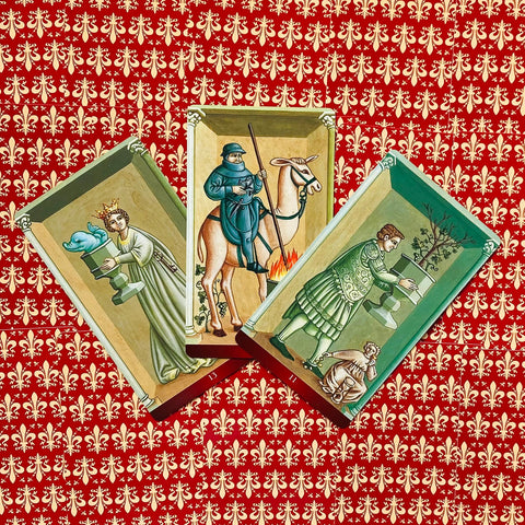 Tarot kortos — trijų istorinių iliustruotų kortų rinkinys ant raudono lelijos raštuoto fono, plokščias išdėstymas