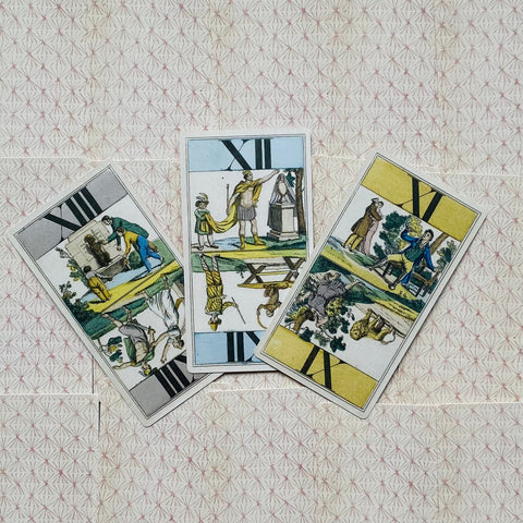 Tarot kortos trijų kortų išdėstymas: tradicinio stiliaus spalvotos kortos, dalis apverstos, ant rausvo ornamentuoto fono