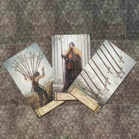 Tarot kortos su Lazdų rūšies iliustracijomis, trys kortos išskleistos fanuotos, centre stovintis IX lazdų simbolis ir detali meninė tekstūra