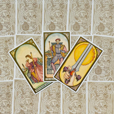 Tarot kortos Rider–Waite stiliaus, trys atvertos kortos fanuotos ant ornamentuotų nugarėlių fono, plokščias išdėstymas