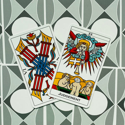 Tarot kortos – Marseille stiliaus Judgement korta virš kitos, ryškios raudonos, mėlynos ir geltonos spalvos, fotografuota iš viršaus ant geometrinio fono