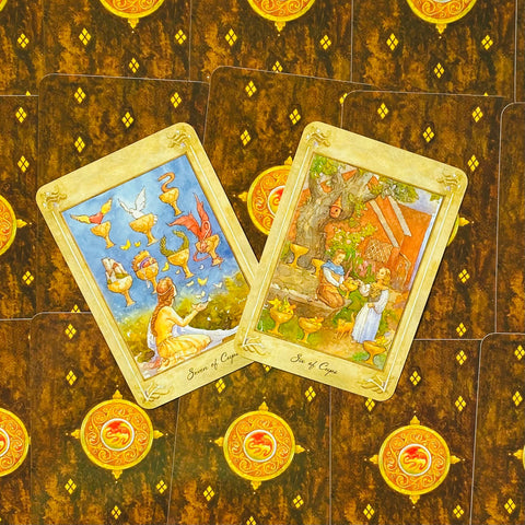 Tarot kortos – dvi atverstos taurų kortos (Six ir Seven of Cups) ant tamsios ornamentuotos nugarėlės