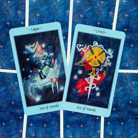 Tarot kortos standardinio dydžio su šviesiai mėlynais borteliais, Ace ir Two of Swords kortos priekinės pusės ant žvaigždėto fono, kampu išdėstytos