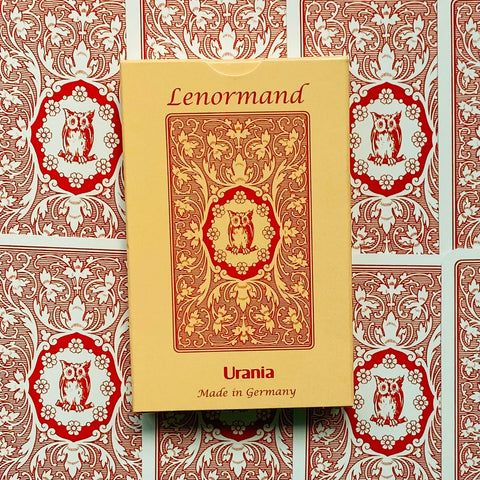 Lenormand kortų rinkinys Urania, smėlio spalvos dėžutė su raudonu ornamentu, padėtas ant raudonų kortų nugarėlių