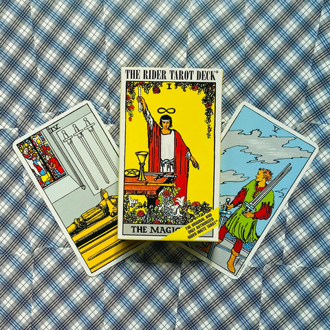 Tarot kortos Rider Waite komplektas su geltonu „The Magician“ dėklu centre ant mėlynos languotos medžiagos, trys atviros kortos