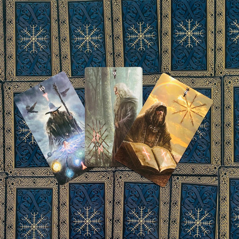 tarot kortos – trys atvertos kortos su mistiniais burtininkų paveikslais ant mėlynos‑auksinės raštuotos nugarėlės