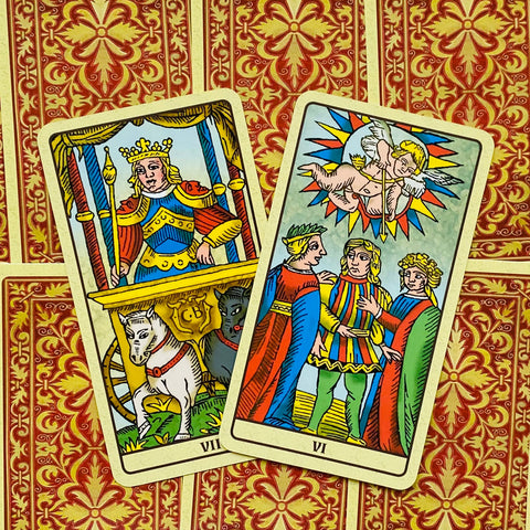 Tarot kortos Marseilio rinkinys, dvi arkos – VII Karieta ir VI Mylimieji, ryškūs spalvoti priekiai ant raudono‑geltono ornamentinio fono
