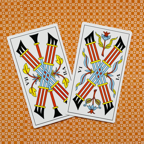tarot kortos (Marseille stilius) – dvi atviros VII lazdelės su raudonomis lazdomis, mėlynais pynimais ir geltonomis detalėmis ant oranžinio rašto fono