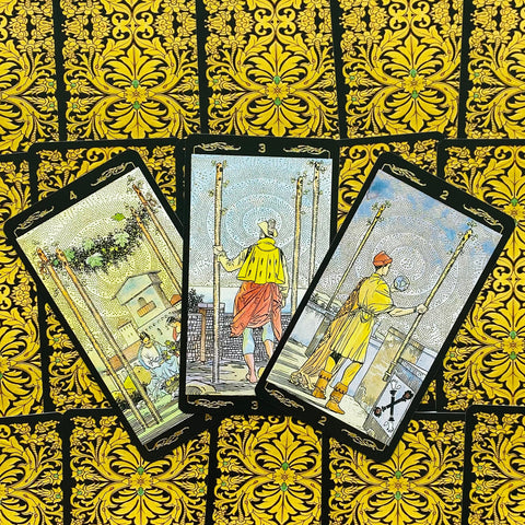 Tarot kortos Rider–Waite komplektas, trys Lazdų rūšies kortos išskleistos ant auksinių ornamentuotų nugarėlių