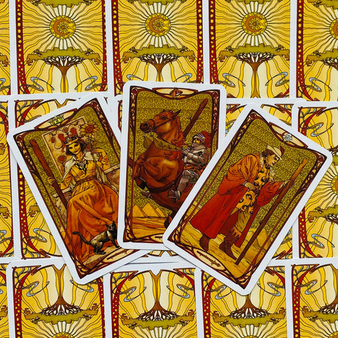 tarot kortos Art Nouveau stiliaus rinkinys — trys atvertos kortos su šiltomis ruda‑auksinėmis iliustracijomis ant geltonų nugarėlių