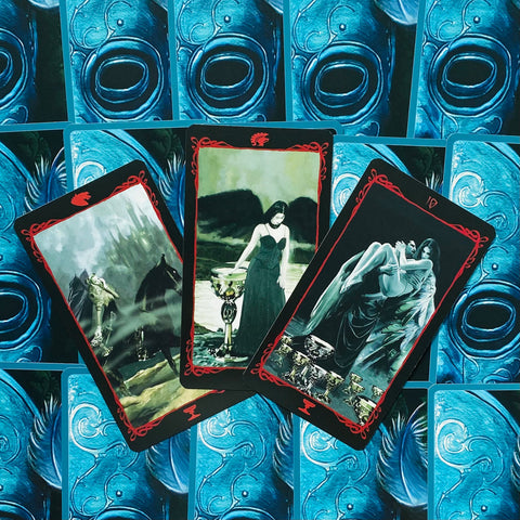 tarot kortos su tamsių iliustracijų trijų kortų išdėstymu ant mėlynų nugarėlių, pabrėžiančios taurės motyvą