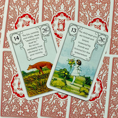 Lenormand kortos su raudonomis nugarėlėmis, dvi priekio kortos išklotos (13 – mergaitė, 14 – lapė), rodo detalią iliustraciją