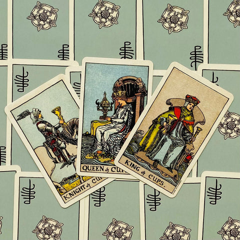 Tarot kortos Rider–Waite stiliaus rinkinyje trys atvertos taurų kortos (Riteris, Karalienė, Karalius) ant mėtų nugarėlių