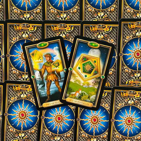 Tarot kortos prabangiu auksiniu rėmeliu, rodomos Pentaklių tūzas ir dvejetukas ant mėlynos ornamentuotos nugarėlės