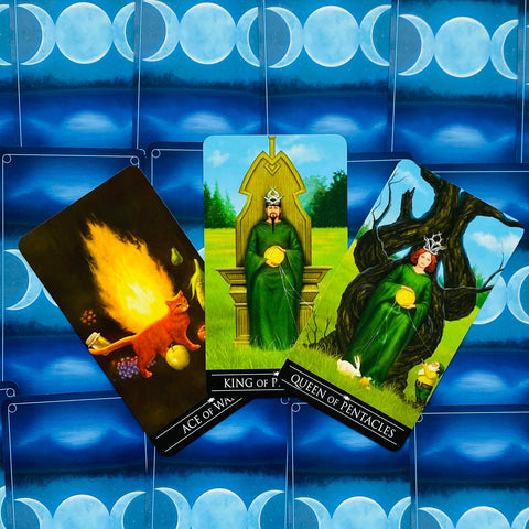 Tarot kortos trijų kortų išklotinė: King of Pentacles centre, Queen of Pentacles dešinėje ir Ace of Wands kairėje ant mėlyno mėnulio fono