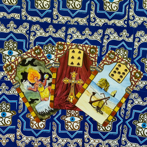 Tarot kortos atverstos trijų kortų kompozicijoje: aukso kryžius, inkaro paplūdimio scena ir liepsnojanti figūra, mėlynos nugarėlės