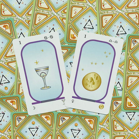 Tarot kortos su taurės ir monetos simboliais, pastelinės mėlynos kortos su purpuriniu rėmeliu ir auksiniu ženkleliu