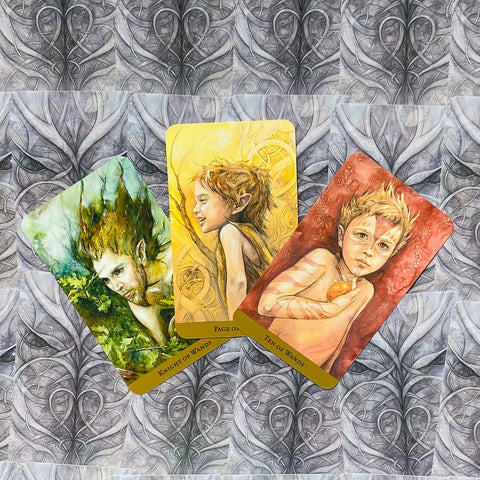tarot kortos trijų kortų komplektas su žalia, geltona ir raudona fėjų iliustracijomis ant pilko ornamentuoto fono