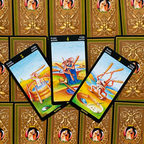 Tarot kortos, iliustruotas variantas: trys atverstos lazdų kortos iš viršaus, parodytos ant auksinės ornamentuotos nugarėlės