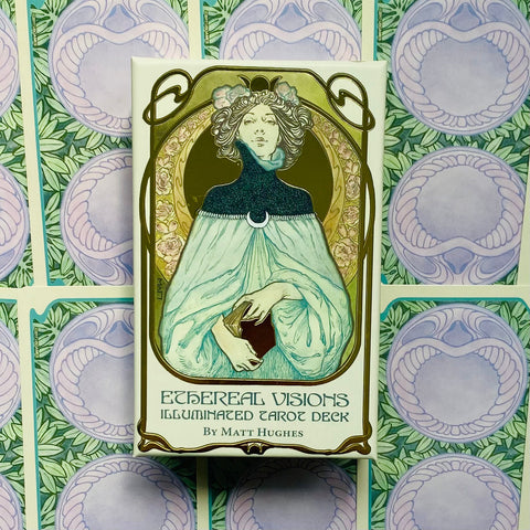 Tarot kortos Ethereal Visions dėžutėje su Matt Hughes iliustracija, žalsvai mėlynu viršeliu ir fonu su kortų nugarėlėmis