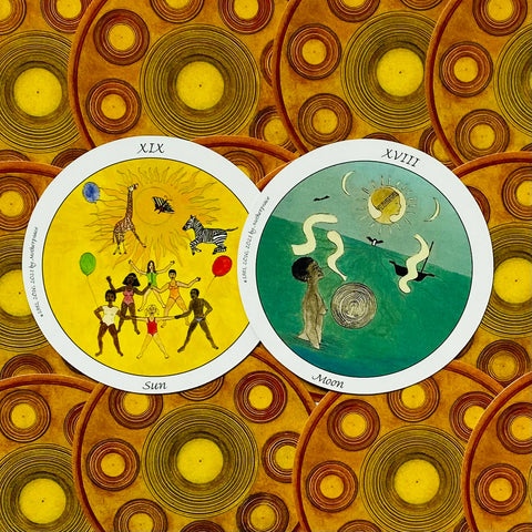 Tarot kortos — atvertos „Sun“ (ryškiai geltona) ir „Moon“ (tamsiai žalsva) kortos ant apvalių, raštuotų nugarėlių, parodytos kartu