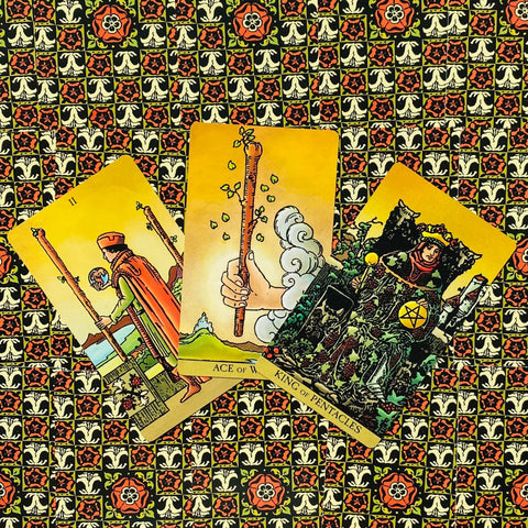 Tarot kortos Rider‑Waite, trijų kortų išklotinė (Ace of Wands, King of Pentacles) ant geltono raštuoto audinio