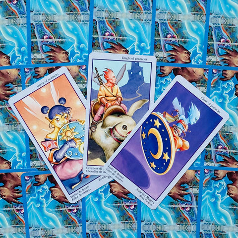 Tarot kortos su trimis Pentaklių kortomis priekyje, ryškiomis iliustracijomis ir mėlyna ornamentuota nugarėle