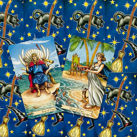 Tarot kortos komplektas: King ir Queen of Cups ant mėlyno fono su geltonomis žvaigždėmis, šluotomis ir juodais katėmis