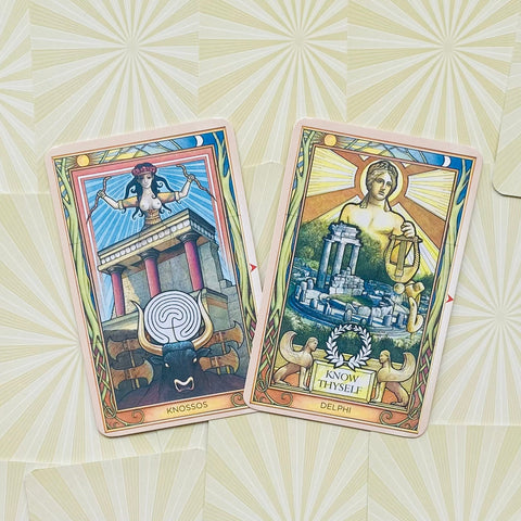 Tarot kortos Delphi ir Knossos su švelniais rožiniais rėmeliais, išdėstytos ant šviesaus spinduliuoto fono, fotografuotos iš viršaus