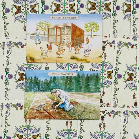 Tarot kortos, dvi kortos (Seven of Swords ir Ten of Swords) su kaimiškais piešiniais ant gėlių rašto fono