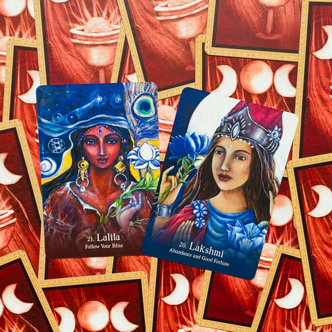 Tarot kortos dvi atverstos Lalita ir Lakshmi kortos su ryškiomis mėlynomis ir raudonomis iliustracijomis, mėnulio nugarėlės fone