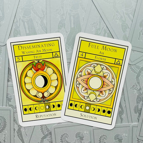 Tarot kortos geltonomis mėnulio iliustracijomis — dvi atverstos kortos (Disseminating ir Full Moon) ant pilko raštuoto fono