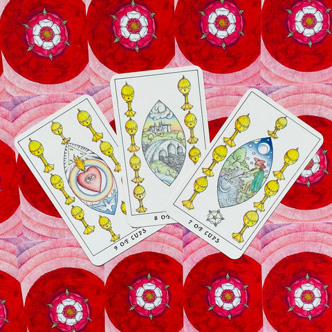Tarot kortos – trys atverstos Puodelių kortos (7, 8, 9) išdėstytos ant raudono ornamentinio fono, akcentuoja kortų simboliką