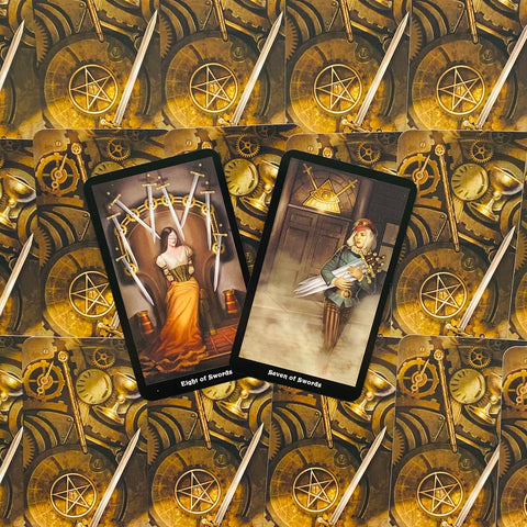 tarot kortos su steampunk auksinėmis nugarėlėmis, dvi atverstos kortos centre (Eight ir Seven of Swords), rodomos priekiniu planu